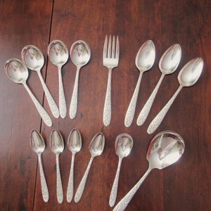 May include: A set of 13 silver-plated spoons and a fork. The spoons are a mix of teaspoons and tablespoons, all with an ornate design. The fork has a similar design.