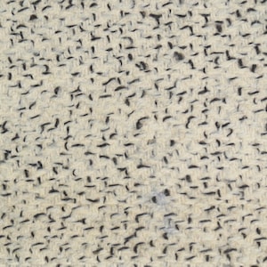 May include: Close-up of a textured fabric with a cream-colored base and scattered black flecks. The pattern creates a woven appearance, suitable for textiles or home decor.