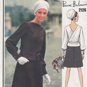 May include: A vintage Vogue Paris Original sewing pattern featuring a design by Pierre Balmain. The pattern number is 2126. The pattern shows two women wearing dresses. One woman is wearing a brown dress with a white belt and a white hat. The other woman is wearing a white blouse with a black skirt and a white hat.