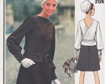 May include: A vintage Vogue Paris Original sewing pattern featuring a design by Pierre Balmain. The pattern number is 2126. The pattern shows two women wearing dresses. One woman is wearing a brown dress with a white belt and a white hat. The other woman is wearing a white blouse with a black skirt and a white hat.