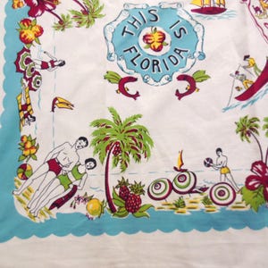 May include: White fabric with a colorful Florida-themed print. The design includes palm trees, people in swimsuits, and the text "THIS IS FLORIDA" in a blue circle. The border is a scalloped light blue.