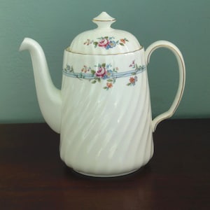 May include: White ceramic coffee pot with a swirling design and floral pattern. The lid has a gold trim and a floral design.