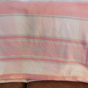 May include: A folded blanket with horizontal stripes in shades of pink, white, and a hint of light blue. The blanket has a soft, textured appearance and a pink border.