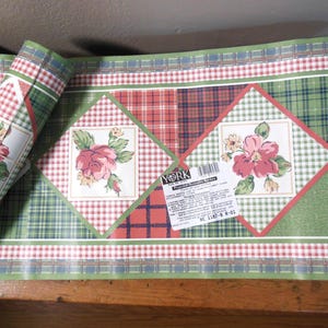 May include: Rolled wallpaper border featuring a repeating pattern of green and red plaid, floral squares, and a red and white gingham border. The design includes pink flowers and a white background.