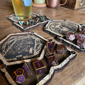 以下が含まれることがあります： 黒と白のダンジョンドアのイラストが描かれた木製ダイス トレイ。トレイには、黒色の数字が書かれた紫と金色のダイスを入れるためのコンパートメントがあります。トレイは、ビールグラスと他のダイスが置かれた木製テーブルの上にあります。
