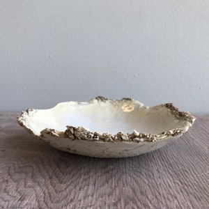 May include: A white ceramic bowl with a rough, textured exterior. The bowl has a wide, shallow shape and a slightly irregular rim.