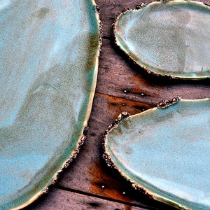 May include: Three ceramic serving platters with a light blue glaze and a rough, textured edge. The platters are oval shaped and have a rustic, handmade look.