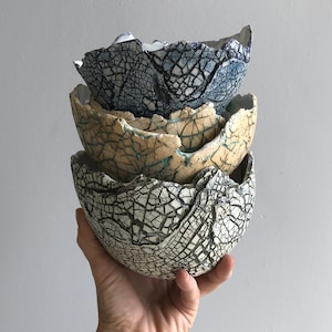 May include: Three ceramic bowls stacked on top of each other. The bowls are all white with a crackled glaze. The top bowl has a blue glaze, the middle bowl has a yellow glaze, and the bottom bowl has a white glaze.