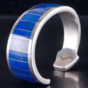 May include: A silver cuff bracelet with a striking design. The bracelet features a series of rectangular blue inlays, creating a bold contrast against the polished silver. The open design allows for easy wear, showcasing a blend of modern and classic aesthetics.