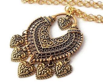 May include: A gold necklace with a large, ornate pendant featuring a heart-shaped design with intricate details and dangling heart charms.