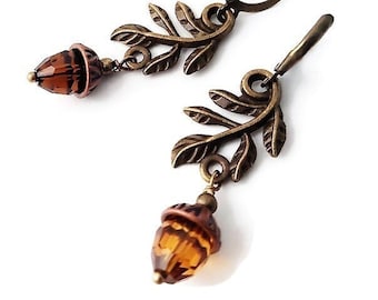 May include: A pair of bronze acorn earrings with amber glass accents. The earrings feature a delicate leaf design with a dangling acorn charm.