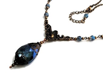 May include: A dark blue crystal pendant necklace with antique bronze filigree accents and a chain of blue glass beads.