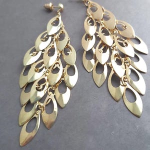 May include: A pair of gold dangle earrings with a cascading design of multiple oval-shaped charms. The charms are connected by small chains and have a cutout design.