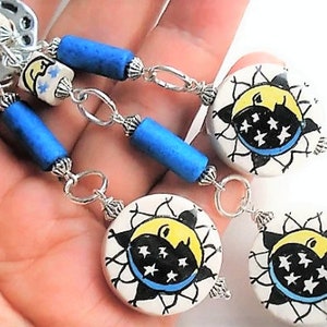 May include: A silver chain necklace with blue and white ceramic beads. The beads feature a sun and moon design with stars.