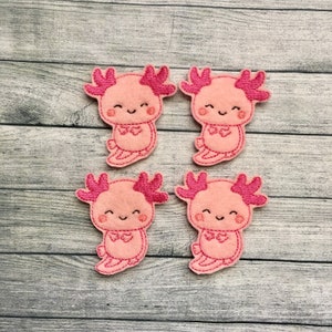 May include: Four pink felt axolotl appliques with pink embroidered details. Each axolotl has a smiling face and a pink bow tie.