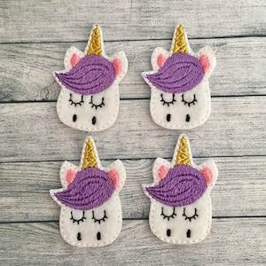 May include: Four white felt unicorn head patches with gold horns, purple manes, pink ears, and closed eyes. The patches are stitched with black thread and have a whimsical, fairytale theme.