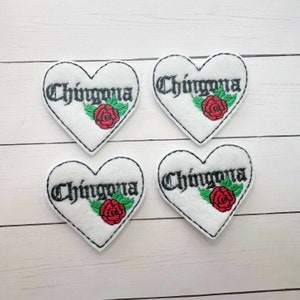 May include: Four white felt heart-shaped patches with black embroidered text that reads "Chingona" and a red embroidered rose with green leaves.