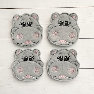 May include: Four gray felt appliques of a hippopotamus face with pink cheeks and black eyes. The appliques are stitched with black and pink thread.