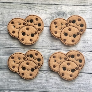 May include: Four sets of felt cookie appliques. Each set features three smiling cookies with chocolate chip details and stitched outlines. The cookies are light brown with dark brown accents.