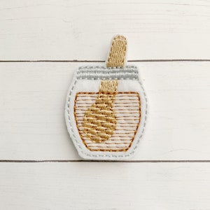 May include: A white felt honey jar with a gold embroidered honey dipper and a gold embroidered lid.
