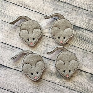 May include: Four gray felt mouse appliqués with black eyes, pink noses, and long tails. Each mouse is outlined with gray stitching. The appliqués are arranged on a light gray and white wooden surface.