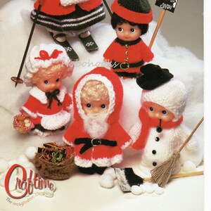 May include: A vintage craft pattern featuring knitted Christmas Tickle Tums dolls. The dolls are dressed in festive outfits, including a skier, Santa Claus, and a snowman. The pattern includes the text "Christmas Tickle Tums" and "Let it Snow".