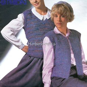 Könnte beinhalten: Zwei Frauen tragen gestrickte Westen. Die Weste links ist gestreift in Blautönen, Lila und Rot. Die Weste rechts ist einfarbig blau. Beide Westen haben einen V-Ausschnitt und sind ärmellos. Die Frau links trägt ein weißes Hemd und ein rosa Stirnband. Die Frau rechts trägt ein helllila Hemd und eine hellblaue Mütze.