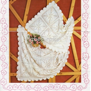 Puede incluir: Una manta de bebé de ganchillo blanco con un patrón de encaje. La manta está drapeada sobre un marco de madera y tiene un borde festoneado. El número de patrón es 13100 y el título es "Robin Double Knitting Bambino".