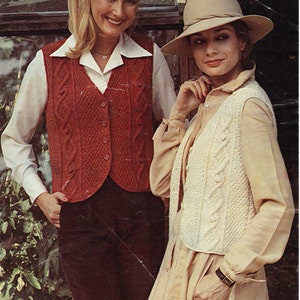 Könnte beinhalten: Zwei Frauen tragen Strickwesten. Die Frau links trägt eine rote Weste mit einem Zopfmuster. Die Frau rechts trägt eine weiße Weste mit einem Zopfmuster. Beide Westen haben einen Knopfverschluss. Der Text "Aran 81-97 cm bust 32-38 ins" ist in der oberen rechten Ecke des Bildes sichtbar.