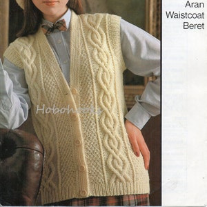 May include: A cream colored Aran knit waistcoat with a cable knit pattern and button closure. The waistcoat is being modeled by a person wearing a cream colored beret and a white shirt with a bow tie. The image also includes the text "Sirdar" and "Aran Waistcoat Beret".