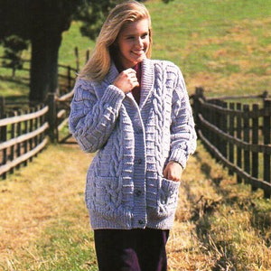 Puede incluir: Una mujer lleva un cárdigan de punto azul claro con cuello chal y bolsillos. Está caminando por un sendero con una valla de madera a cada lado.