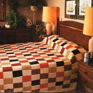 Könnte beinhalten: Eine karierte Bettdecke in Braun-, Rot-, Schwarz- und Cremetönen. Die Bettdecke liegt auf einem Bett mit einem Holz-Kopfteil und einem braunen Nachttisch mit Schubladen.