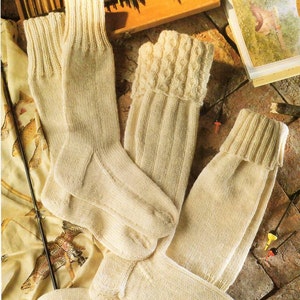 Puede incluir: Cuatro pares de calcetines de punto de color crema con diferentes patrones. Los calcetines están doblados y dispuestos sobre una superficie de ladrillo marrón.