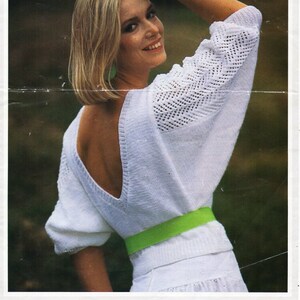 May include: A white knitted sweater with a low back and a green belt. The sweater has a lacy pattern on the sleeves. The model is wearing the sweater with a white skirt. The pattern number is 13476, and the size is 32-40 inches.