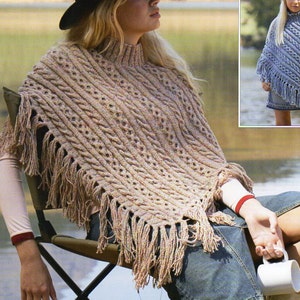 Könnte beinhalten: Eine Frau trägt einen braunen und beigefarbenen Strickponcho mit Fransen. Der Poncho hat ein Zopfmuster. Die Frau sitzt auf einem Klappstuhl mit einer Tasse in der Hand. Der Hintergrund ist ein See und grünes Gras. Das Bild zeigt auch ein Mädchen, das einen blauen Strickponcho mit Fransen trägt. Das Bild enthält den Text "Donegal Tweed DK" und "8456 7 years to adult".