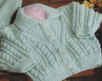 May include: A set of knitted baby clothes in cream and light green. The set includes a hooded sweater, a cardigan, a hat, and mittens. The sweater has a cable knit pattern and the cardigan has a button closure. The hat and mittens are also cable knit.