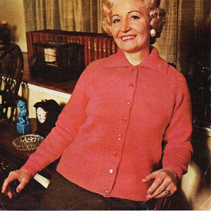 May include: A pink knitted cardigan with a button fastening. The cardigan is being modelled by a woman with blonde hair. The text on the image reads "ROBIN TRICEL-NYLON and all Double Knitting to fit 34 to 44 bust 1661 8p".