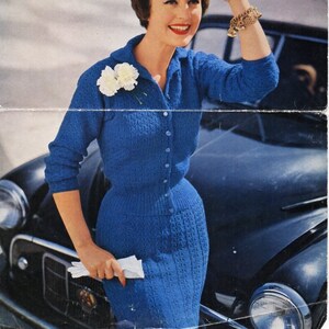 Peut inclure: Une femme portant une robe et un cardigan en tricot bleu, debout à côté d'une voiture. La robe et le cardigan ont un motif texturé. La robe a un devant boutonné. La femme tient un mouchoir en papier blanc dans sa main. L'image contient le texte "Campanula 3 ply and Leemont Double Crepe", "MOTHPROOFED", "BUST 34"-36"", "1377", et "6d".