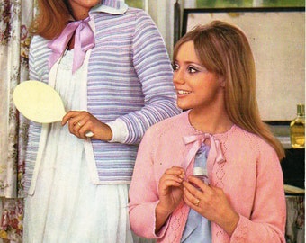 May include: Two women wearing knitted cardigans. The woman on the left is wearing a striped cardigan with a pink bow and a white dress. The woman on the right is wearing a pink cardigan with a pink bow and a blue dress. The image includes the text "PATONS yarns of various weights" and "SC107 1/6d".
