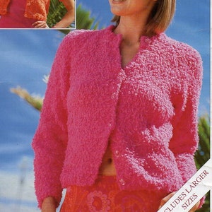 May include: A pink knitted cardigan with a chunky texture. The cardigan has a V-neck and short sleeves. The model is wearing the cardigan over a floral print top. The text "INCLUDES LARGER SIZES" is visible in the bottom right corner of the image.