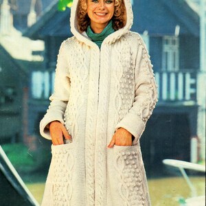 May include: A white knitted hooded cardigan with a cable knit pattern and a zip closure. The cardigan has pockets and a long length.