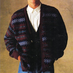 May include: A man wearing a dark red, blue, and black patterned cardigan with a white button-down shirt underneath. The cardigan has a knit texture and a v-neck. The man is wearing blue jeans.