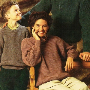 Op de afbeelding: Een gezin van drie personen draagt gebreide truien. De vader draagt een groene trui, de moeder draagt een roze trui en de zoon draagt een paarse trui. Ze zitten op een houten bank voor een bruine en gouden achtergrond met een patroon.