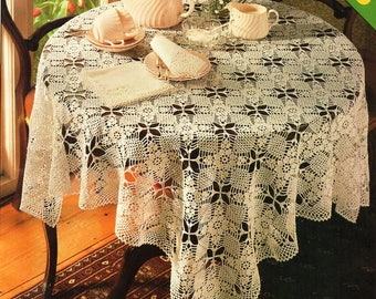 May include: A white crocheted tablecloth with a delicate floral pattern, set on a round wooden table with a teapot, creamer, and cups. The tablecloth has a scalloped edge and is made with a fine yarn.