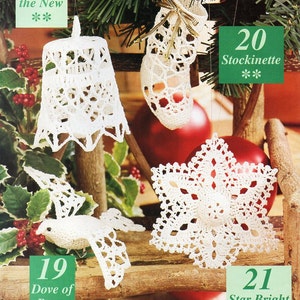 May include: Four crocheted Christmas ornaments: a bell, a stocking, a dove, and a star. The ornaments are white and hang from a wooden branch.