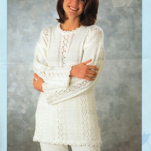 May include: A white knitted jumper with a lace pattern. The jumper has a round neckline and long sleeves. The model is wearing the jumper with her arms crossed.