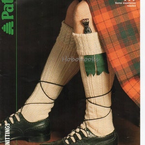 Puede incluir: Un par de calcetines blancos de punto con un borde de cable y nervaduras. Los calcetines se llevan con zapatos de cuero negro y una falda escocesa. La imagen incluye el texto "CODE C 3285 TO FIT FOOT SIZE 25-28 cm 10-11 in Some experience needed".