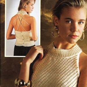 May include: A white sleeveless top with gold beads throughout the fabric. The top has a high neckline and a criss-cross back design.