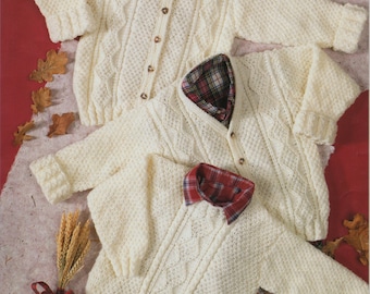 May include: Two white knitted sweaters with cable knit patterns. The sweaters have button closures and are laid out on a brown surface with red and brown leaves.
