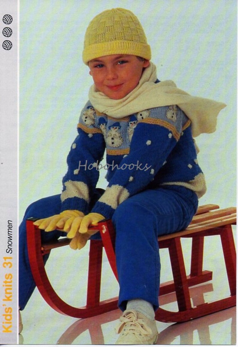 May include: A child wearing a yellow knit hat, scarf, gloves, and a blue sweater with snowman designs, sitting on a red sled. The sweater has white and blue accents. The child is also wearing blue pants and white sneakers.